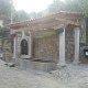 Construção tradicional com pérgola em madeira, poço ou tanque de água em pedra, e paredes brancas num cenário rural.
