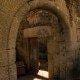 Arco medieval de pedra com porta de madeira aberta, deixando passar luz solar.