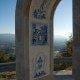 Estrutura de arco em pedra com painéis de azulejos azuis de temática religiosa, enquadramento de vale e montanhas ao fundo.