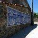 Painel de azulejos azuis e brancos com cena de igreja e paisagem rural português numa parede de pedra