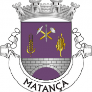Brasão de Matança com coroa almofadada, escudo púrpura com ferramentas agrícolas e milho, e listras laterais.