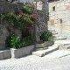 Rua de pedra com escadas, muros antigos de granito e flores vermelhas em jardineiras.