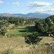 Vale agrícola com campos cultivados, vegetação densa e serras ao fundo sob céu nublado.