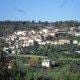 Vista panorâmica de vila com habitações dispersas em encosta, verde agrícola envolvente e árvores.