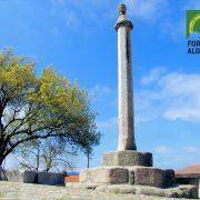 Pelourinho de pedra com fuste alto e capitel, estrutura base em blocos de granito, árvore ao fundo, logo Fornos de Algodres. — ampliar imagem