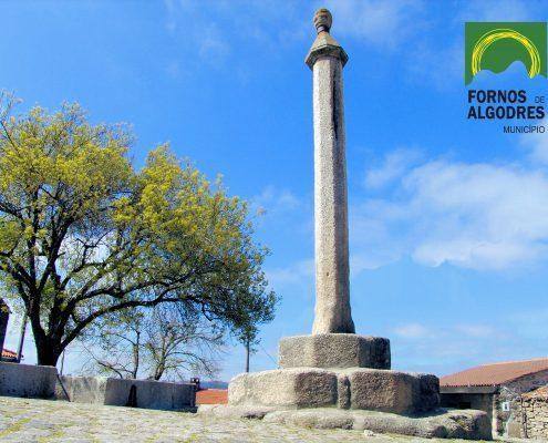 Pelourinho de pedra com fuste alto e capitel, estrutura base em blocos de granito, árvore ao fundo, logo Fornos de Algodres. — ampliar imagem