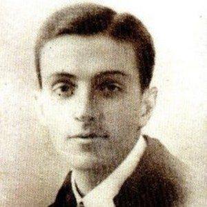 Homem adulto de rosto alongado em retrato de busto, cabelo escuro penteado para trás, usando casaco escuro.