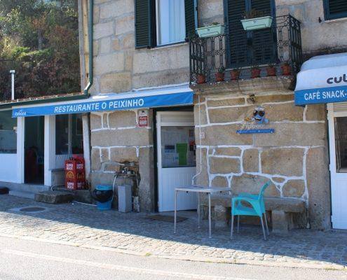 Fachada de restaurante e café com painel azul, entrada branca e cadeira turquesa na rua de calçada portuguesa.