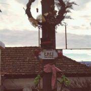 Cruzamento com poste central vermelho decorado com coroa de ramos e laço rosa, edifícios tradicionais ao fundo.