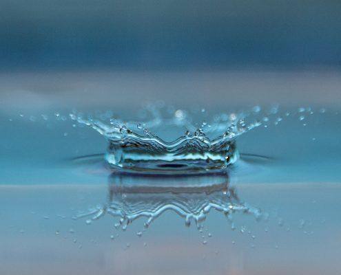 Coroa de água formada por respingo simétrico numa superfície líquida com fundo azul