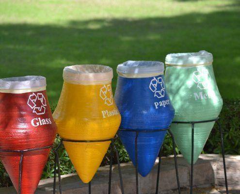 Quatro cones de reciclagem coloridos com rótulos para vidro, plástico, papel e metal, sobre estacas no jardim