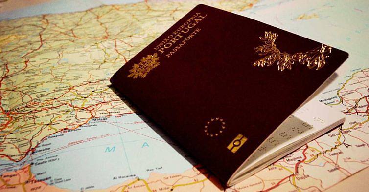 Passaporte português em tom castanho colocado sobre mapas de estradas em cores variadas.