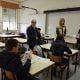 Adultos apresentam projeto em sala de aula com alunos sentados às mesas