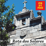 Fachada de Igreja de pedra com cruz no topo, sinos e brasão heráldico, sob céu azul. — abre num novo separador