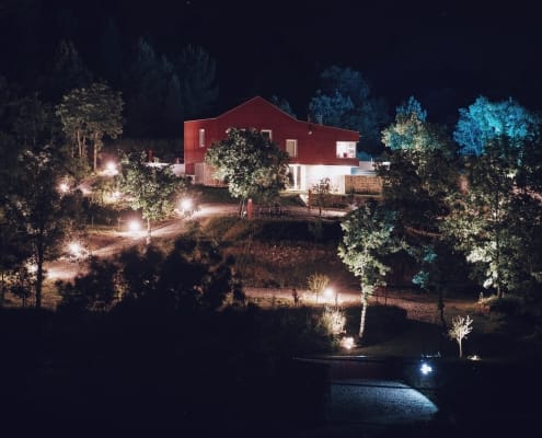 Casa moderna iluminada à noite rodeada por árvores com sistema de lighting de jardim, próxima a linha de água.