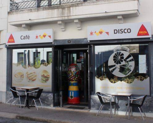 Fachada de café-disco com sinalética Delta, vitrines decoradas e mesas de esplanada