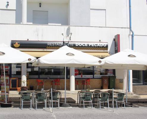 Fachada de restaurante com toldo preto e bege, esplanada com mesas e cadeiras cinzentas.