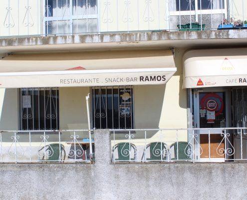 Fachada de restaurante com toldos retraídos, mostrando esplanada com mesas e cadeiras verdes.