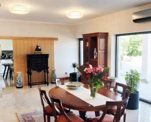 Sala com mesa de madeira, estátua grega, portas de vidro para jardim e flores frescas