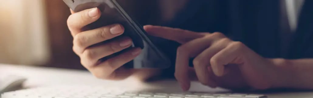 Mãos segurando smartphone sobre superfície branca com iluminação lateral
