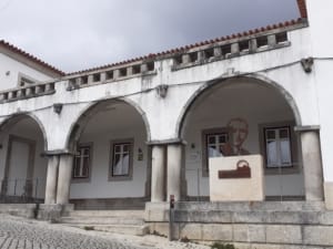 Fachada do Centro Cultural com três arcos de pedra, colunas, painel com retrato e placa identificativa.