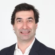 Homem de meia-idade com cabelo escuro, sorridente, em retrato de busto com fundo branco.