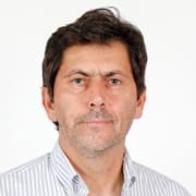 Homem de meia-idade com cabelo escuro, bigode, usando camisa branca às riscas, sobre fundo branco