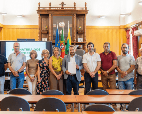 Grupo de pessoas reunidas numa sala institucional com painéis e bandeiras, posando para fotografia.